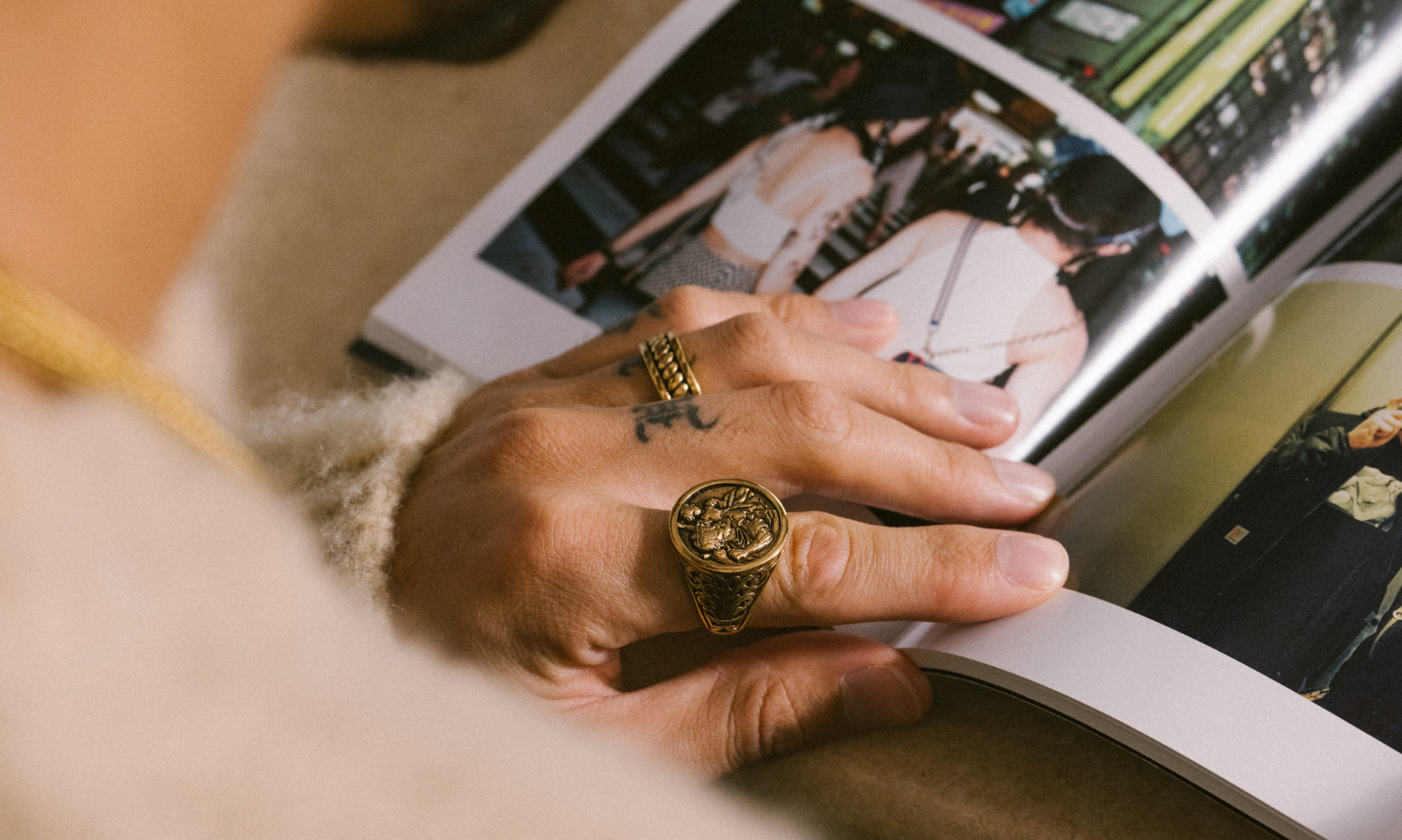 Man flicking through a jewellery style guide book. He's wearing bold gold signet rings