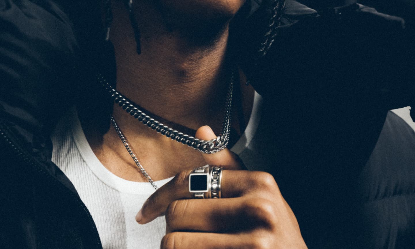 Man wearing a plain white t-shirt and layering a black coat and silver cuban link chain