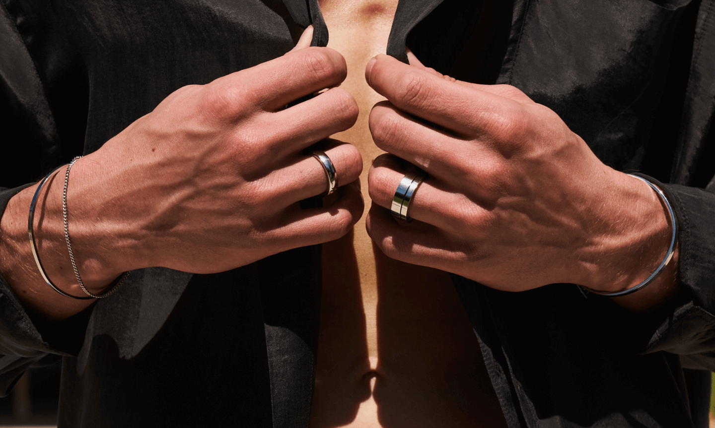 Man wearing a classic open collar black shirt and styling essential silver jewellery including rings, bracelets and bangles