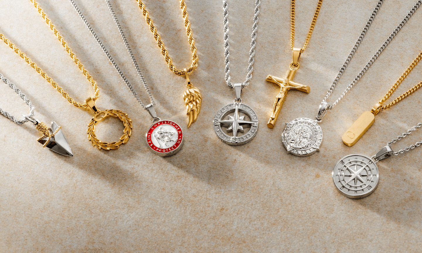 Flat lay of mixed gold and silver pendant necklaces, including compass designs, crosses, angel wings, and laurel wreaths. Each piece reflects a different meaning like faith, direction, strength.