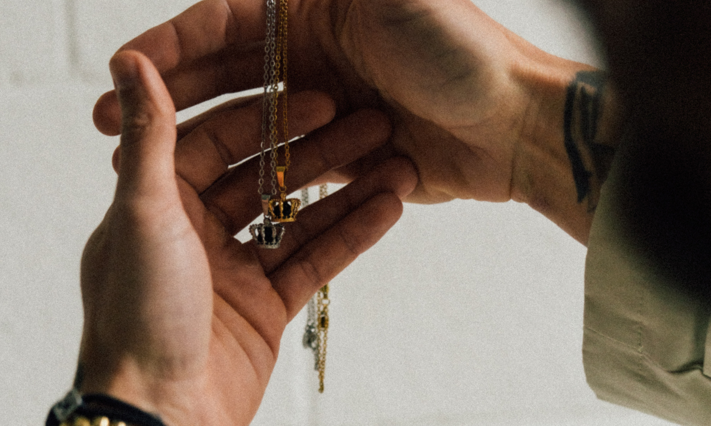 Close up of a man holding two crown Pendants Necklaces. One gold, one silver, both set with black onyx stones. The highest quality and most durable jewellery for men. 