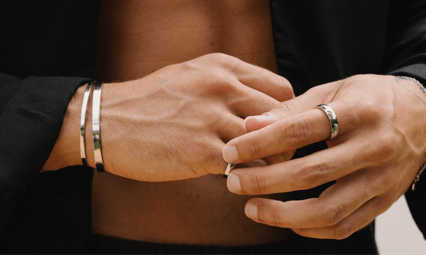 Man wearing simple men's jewellery including a minimal silver cuff bracelet and classic silver rings 