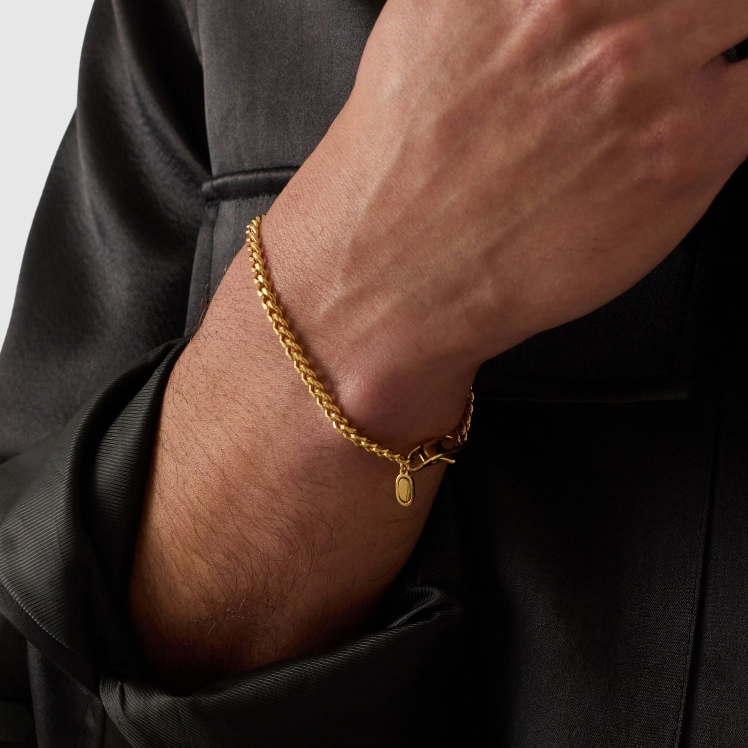 Gold chain bracelet on a person's wrist with a plain background